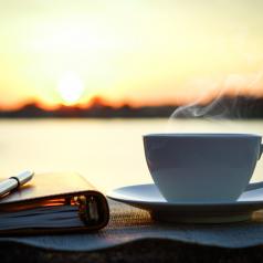 Coffee, journal, and pen on table outside at sunrise
